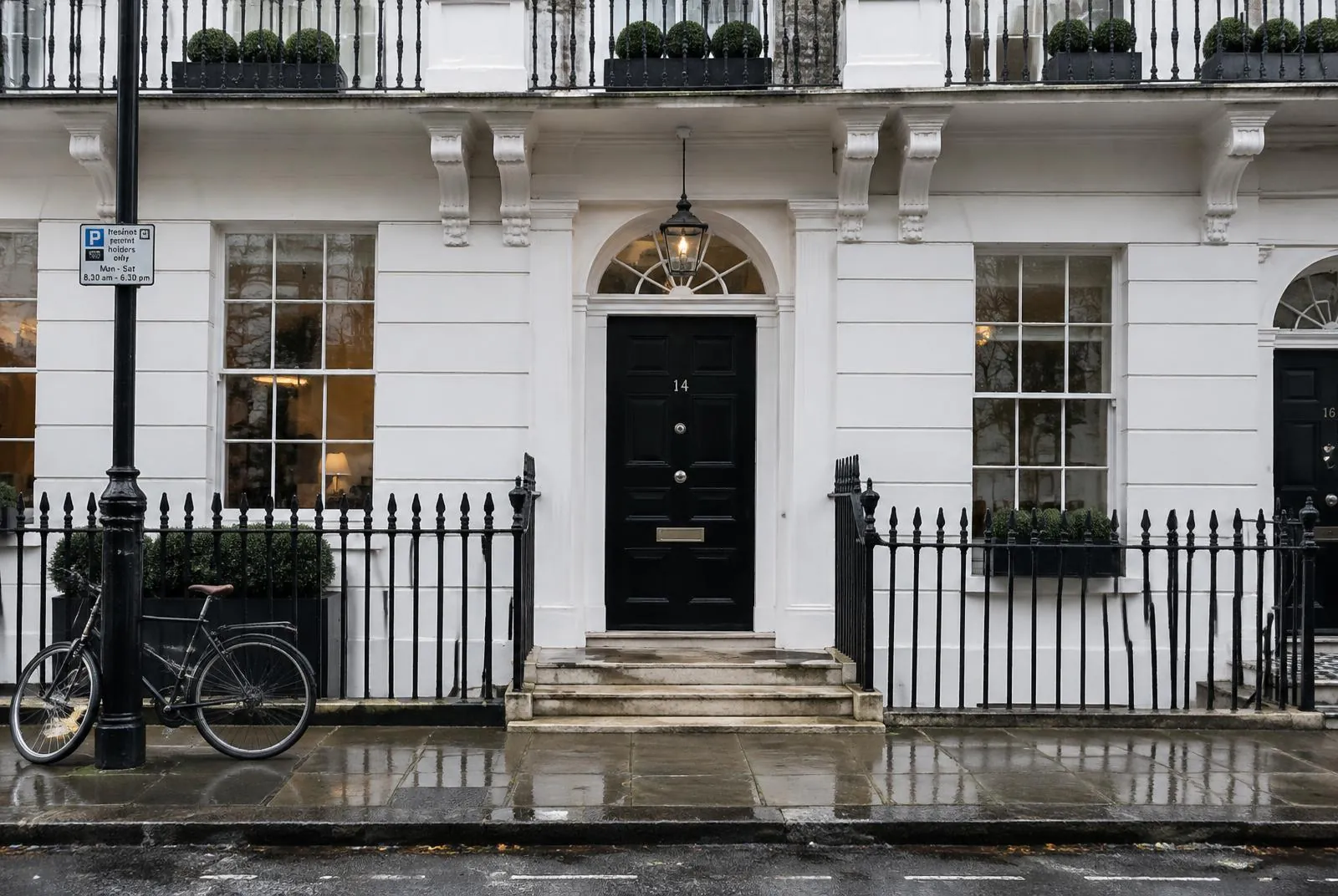 A white stucco London townhouse with a black front door on a wet street
